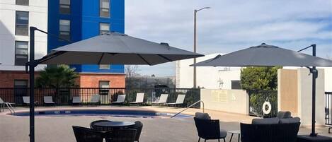 An outdoor patio area with a pool, lounge chairs, and umbrellas.
