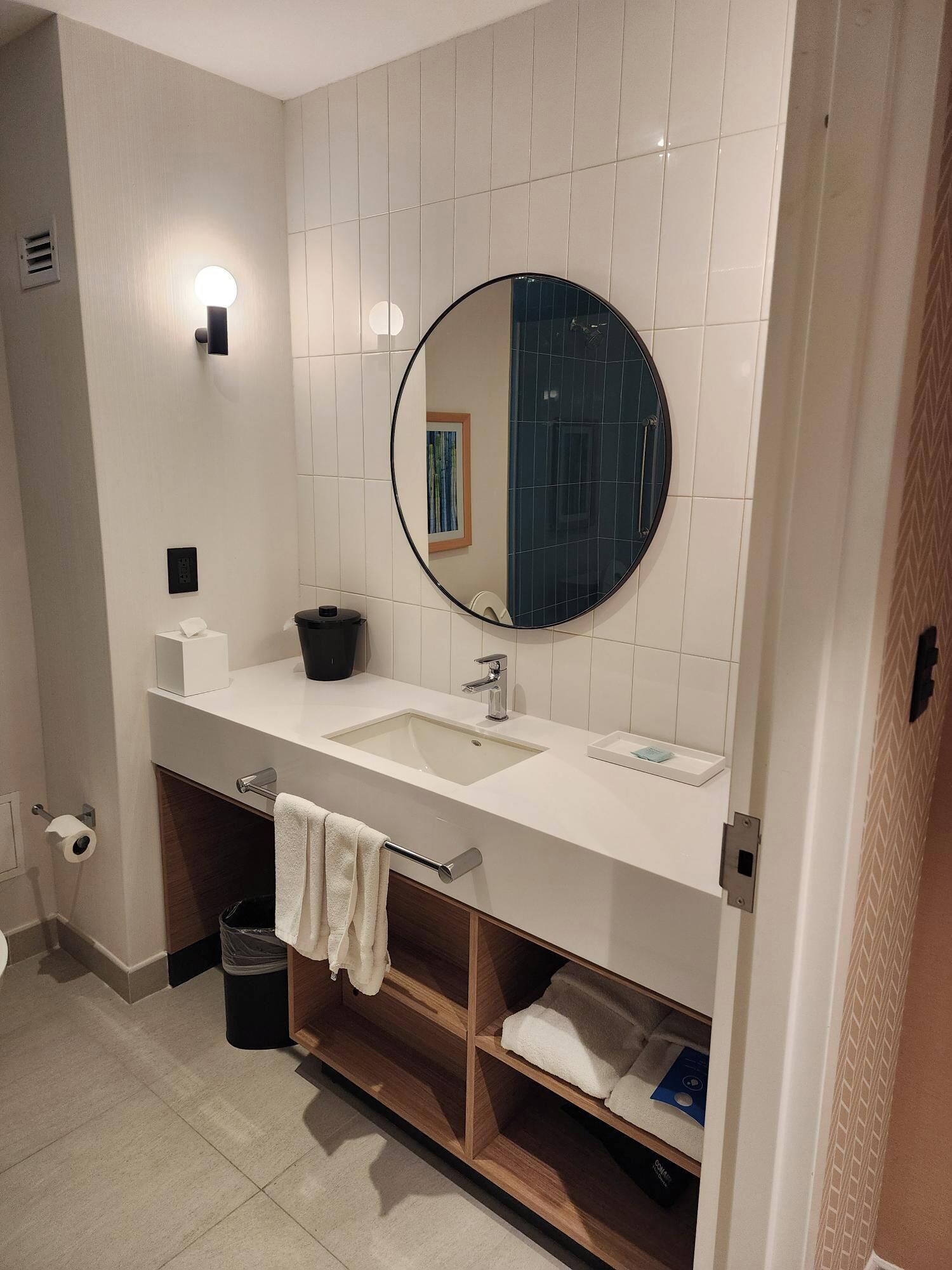 Een moderne badkamer met een witte wasbak, een ronde spiegel en een handdoekrek.