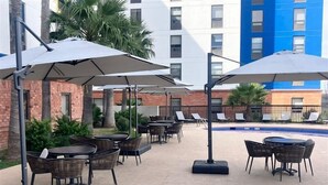 An outdoor patio area with tables and chairs, umbrellas, and a pool. - Hampton by Hilton Saltillo (Saltillo)