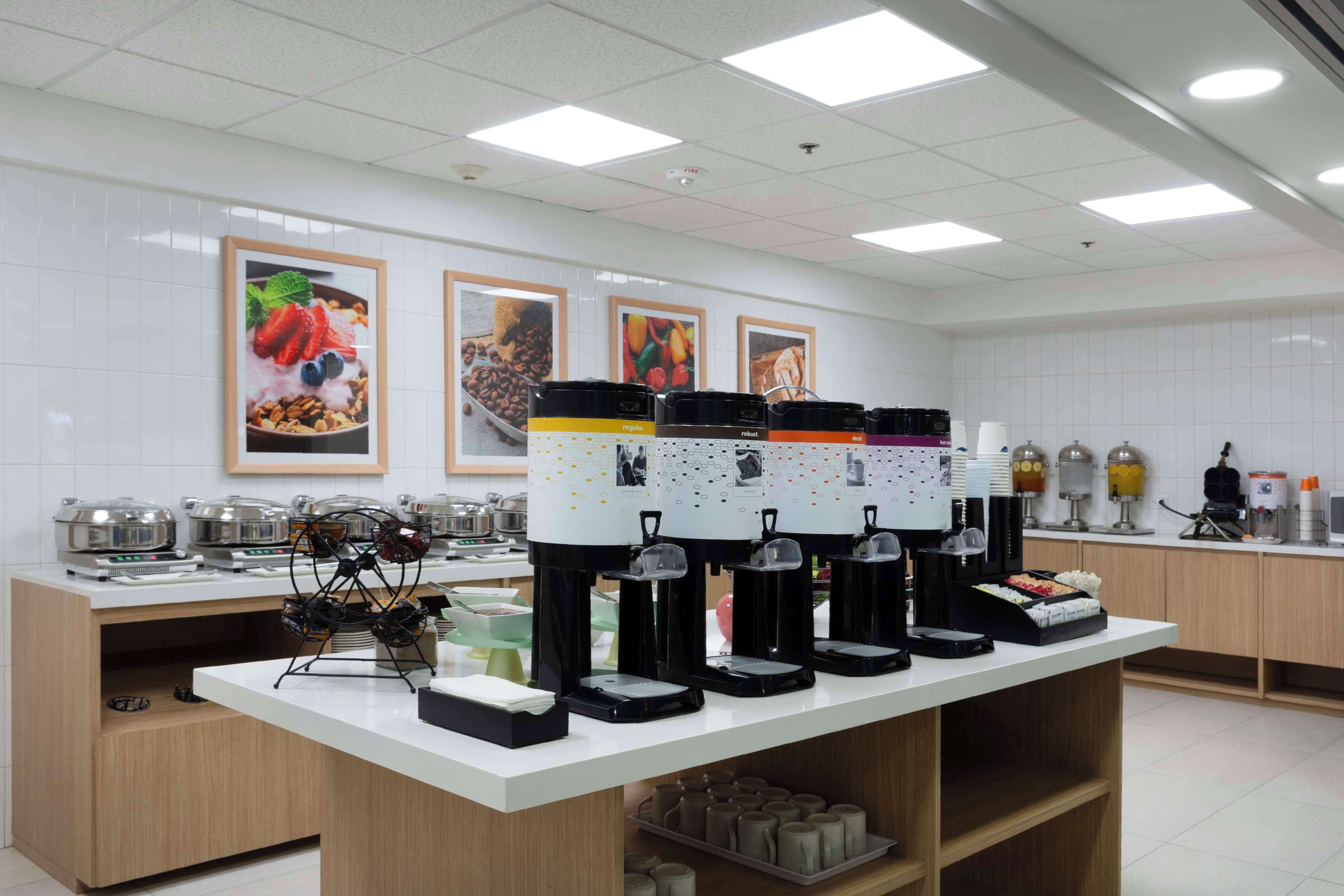 Una barra de desayuno con varios dispensadores de café, una exhibición de frutas y una variedad de electrodomésticos de cocina.