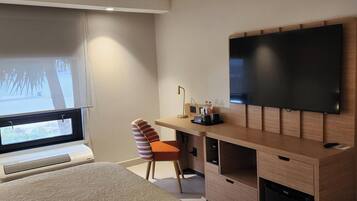 Una habitación de hotel moderna con una cama grande, un escritorio con televisor de pantalla plana, una silla y una ventana con persianas.