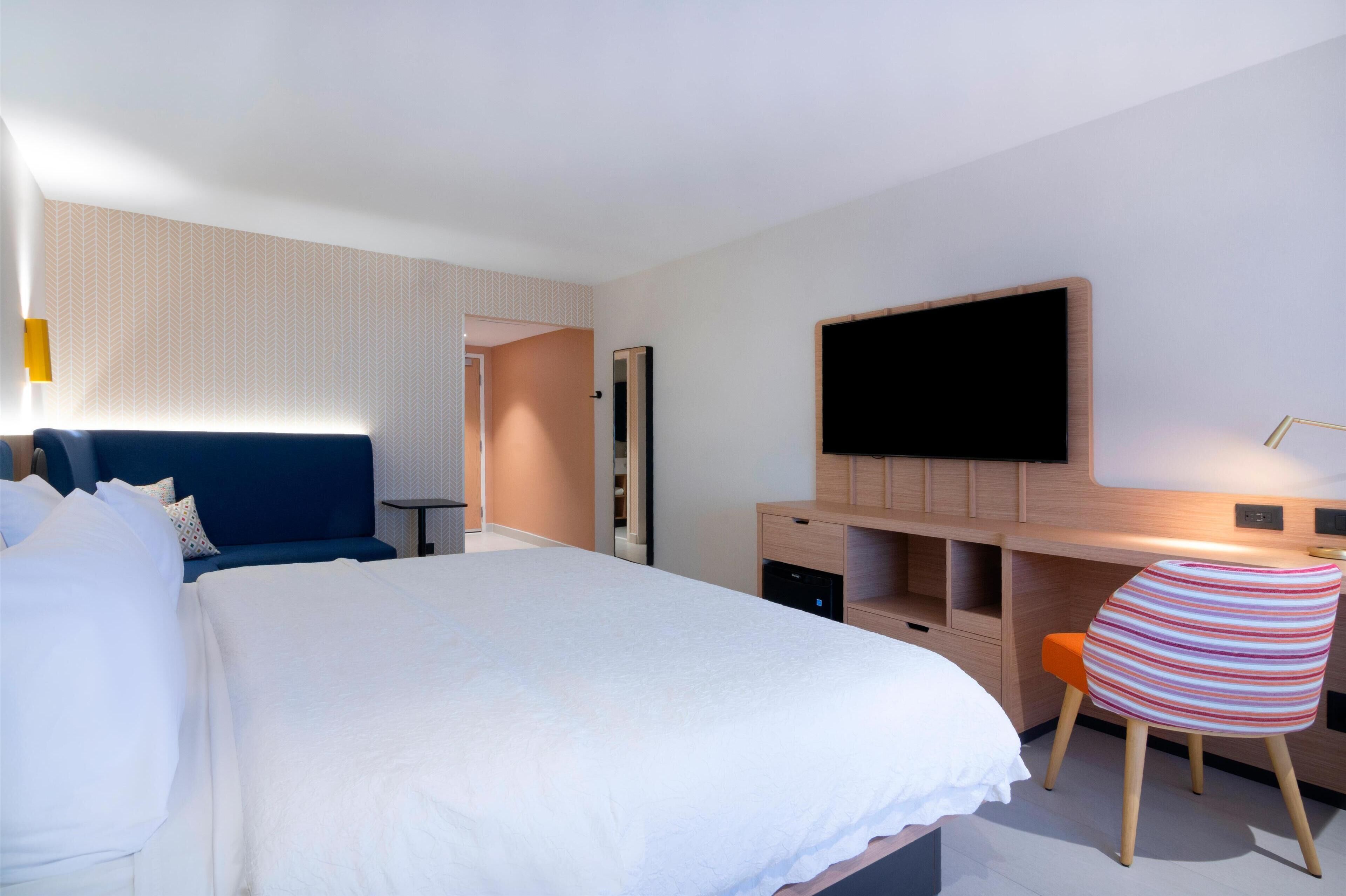 Quarto de hotel moderno com uma cama grande, uma escrivaninha com televisão de tela plana, uma cadeira listrada e um guarda-roupa.