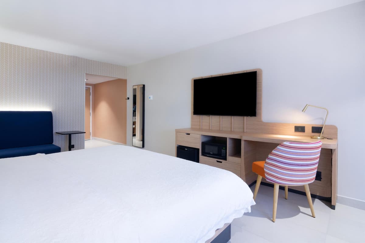 Ein modernes Hotelzimmer mit einem großen Bett, einem Schreibtisch, einem Flachbildfernseher, einer Mikrowelle und einem gestreiften Sessel.