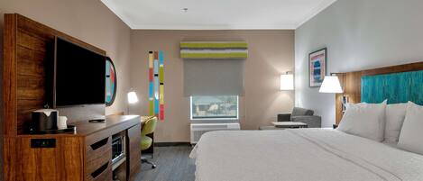 Ein Hotelzimmer mit einem großen Bett, einem Schreibtisch mit Flachbildfernseher, einem Sessel, einer Schreibtischlampe und einem Fenster mit Blick.