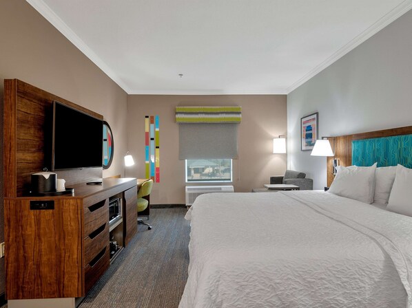 A hotel room with a large bed, a desk with a flat-screen TV, a chair, a desk lamp, and a window with a view.