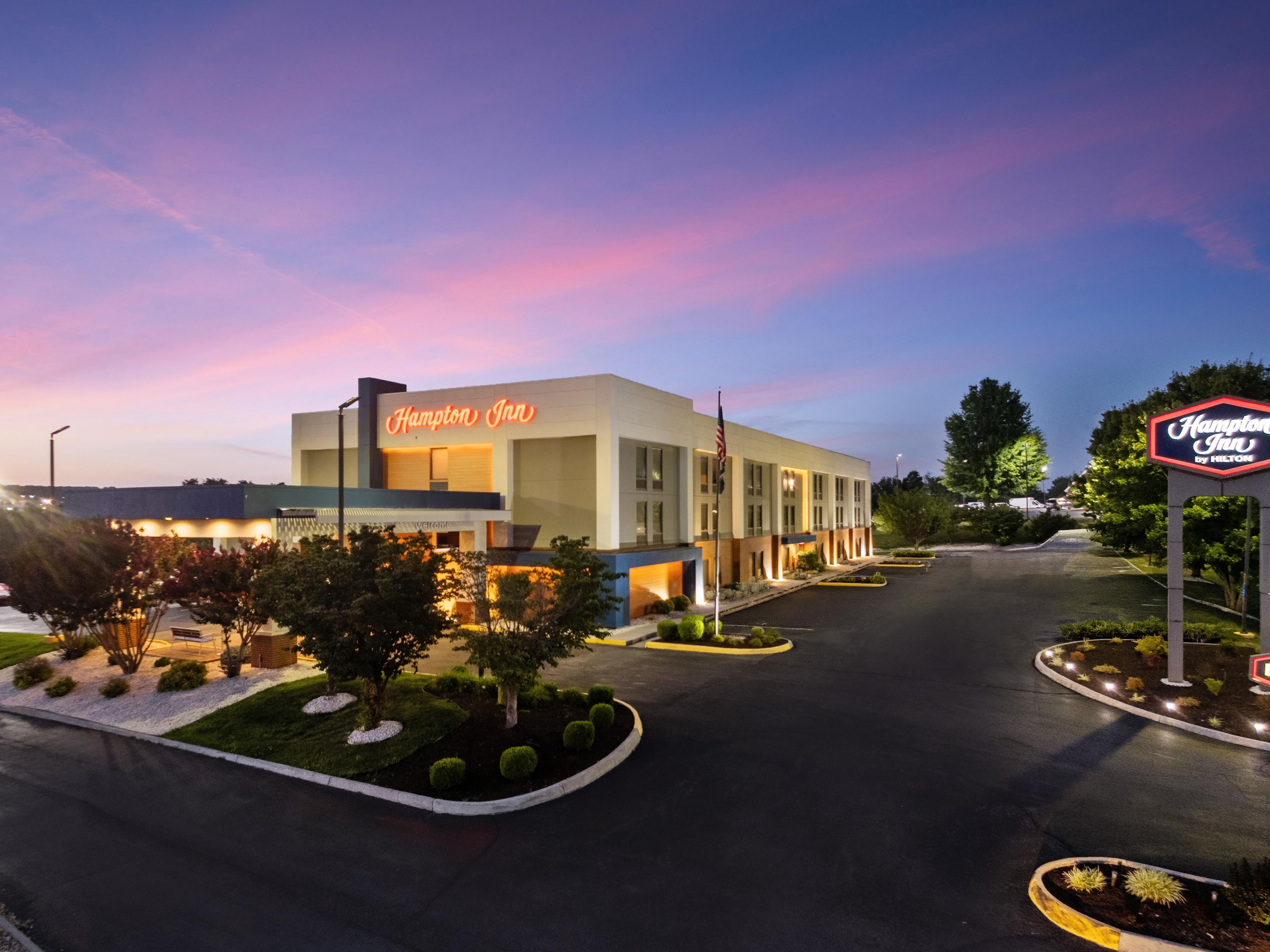 A Hampton Inn hotel with a modern design, featuring a well-lit entrance and a parking area.