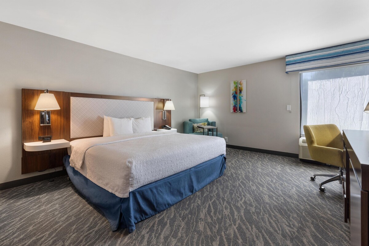 Habitación de hotel con una cama grande, lámparas de noche, un escritorio con silla y una ventana.