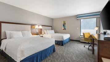 Ein Hotelzimmer mit zwei Betten, einem Schreibtisch, einem Stuhl, einer Lampe und einem Fenster.