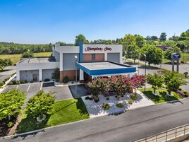 Un hotel Hampton Inn con estacionamiento, un espacio al aire libre techado y un jardín delantero ajardinado.