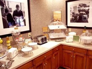 A breakfast bar with a toaster, coffee maker, and a fruit bowl. There are framed pictures on the wall and wooden cabinets below.