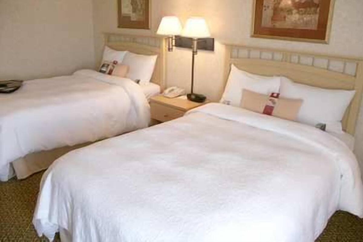 A hotel room with two beds, each with white bedding and pillows, a bedside lamp, and a phone on the nightstand.