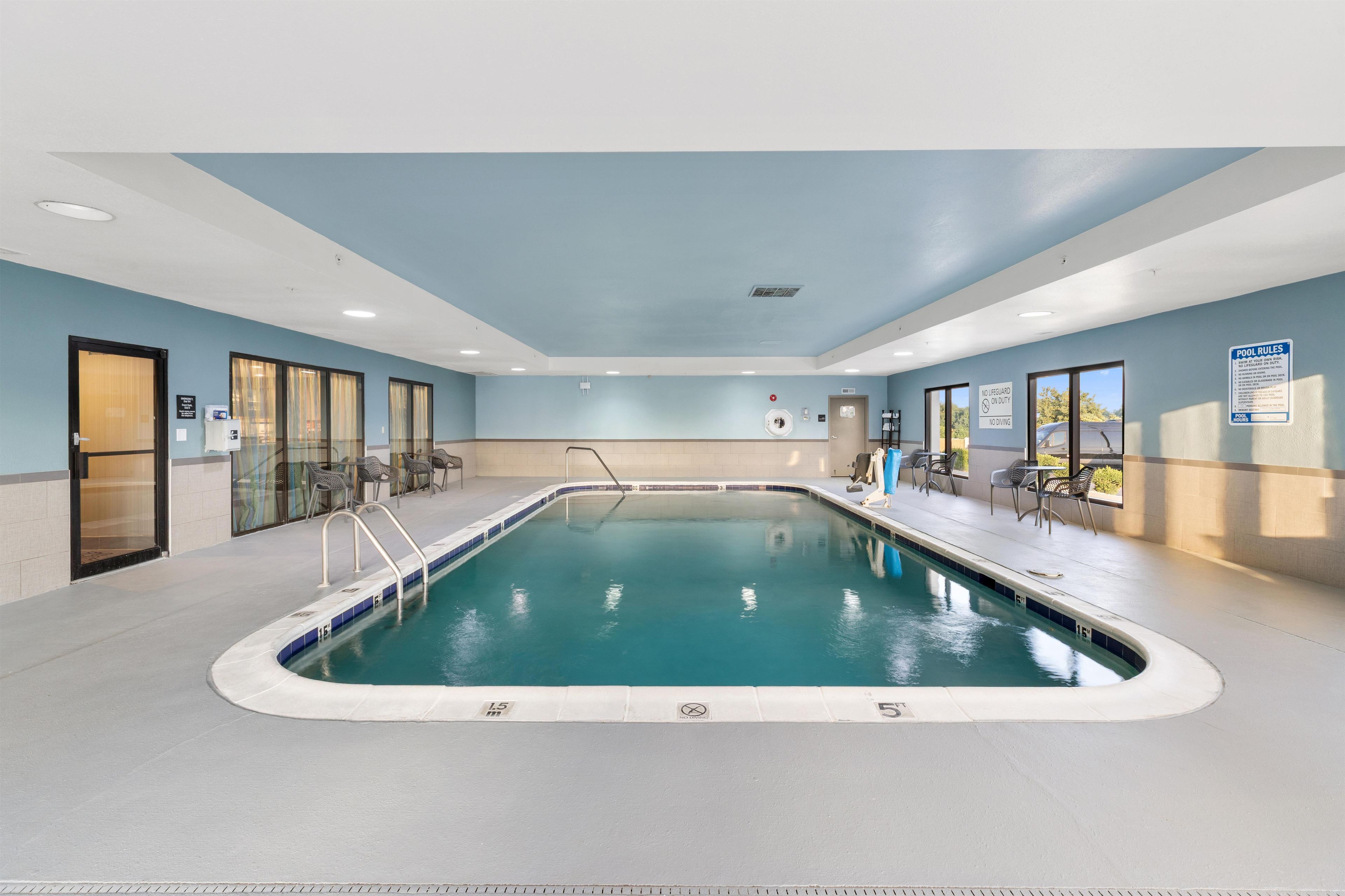 An indoor swimming pool with clear water, a lifeguard chair, and pool rules sign.