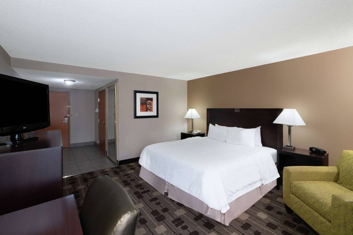 A hotel room with a bed, a desk, a television, a chair, and a lamp.