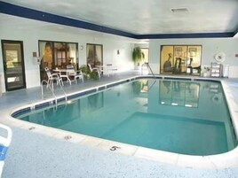 Una piscina interior con agua cristalina, rodeada de sillones blancos y una zona de estar con mesas.