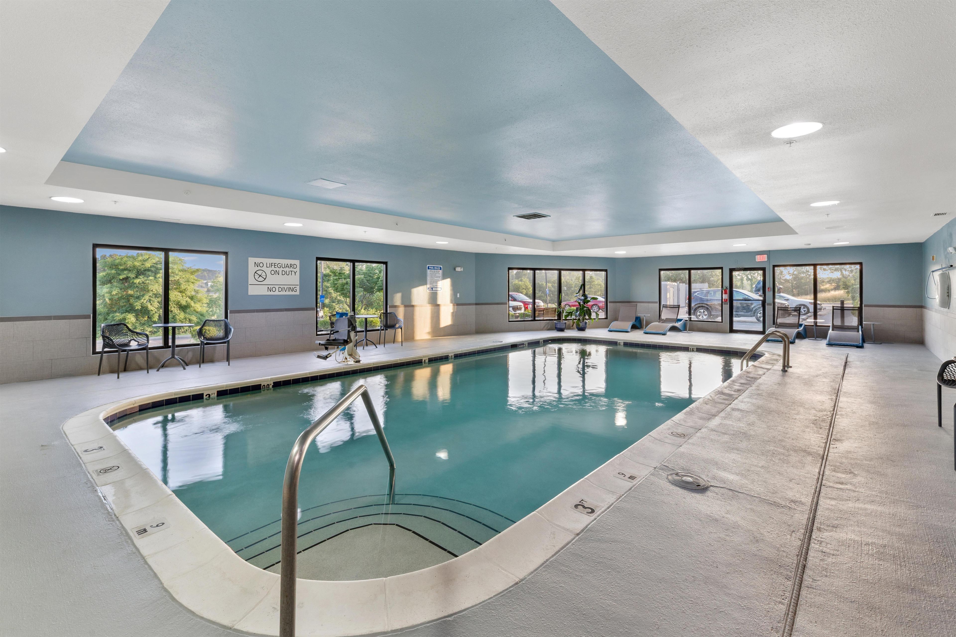 An indoor swimming pool with clear water, a lifeguard station, and a view of the outdoors through large windows.