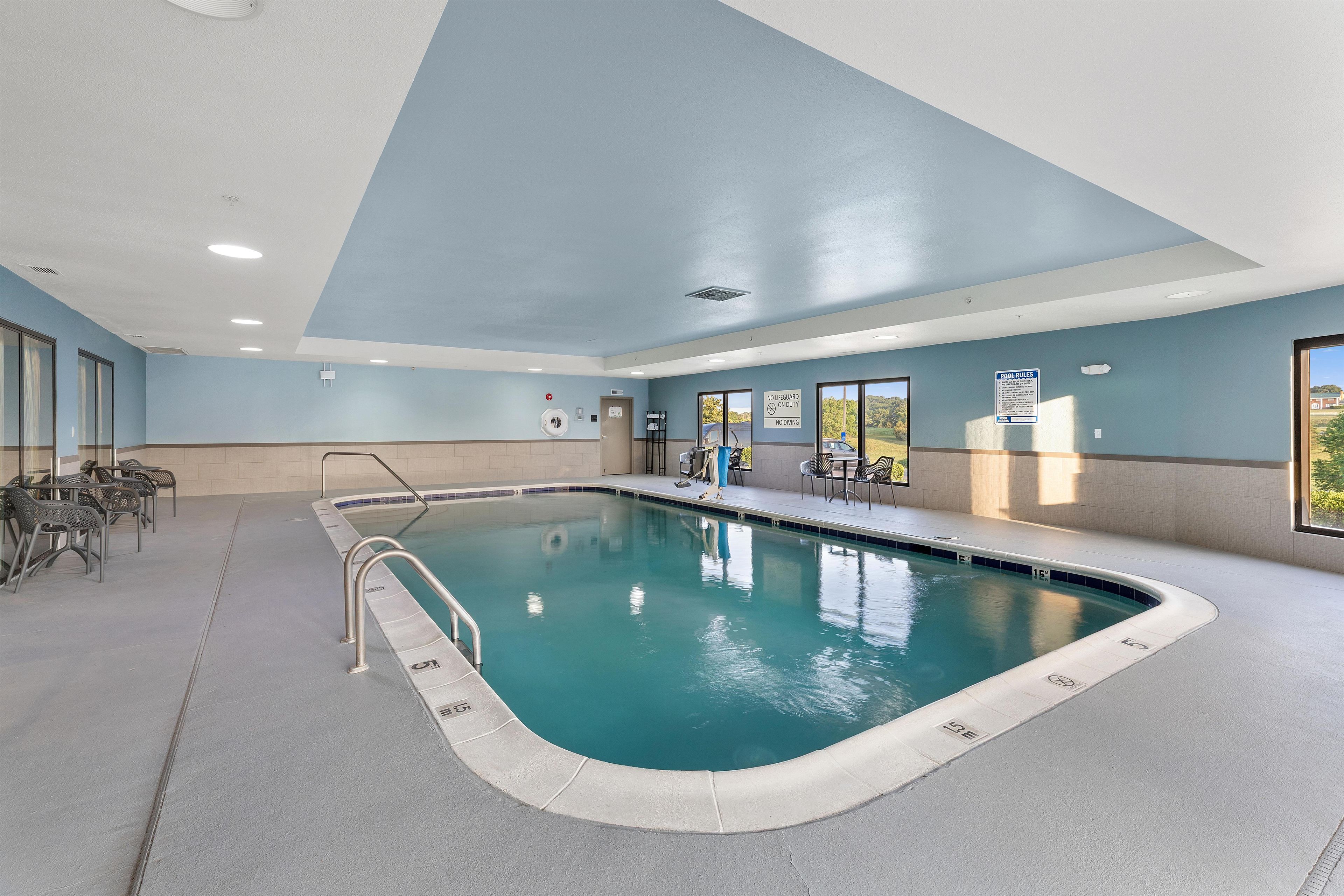 Una piscina interior con agua cristalina, una estación de salvavidas y un cartel con las normas de la piscina.