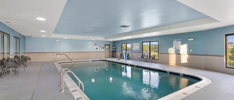 Una piscina interior con agua cristalina, una estación de salvavidas y un cartel con las normas de la piscina.