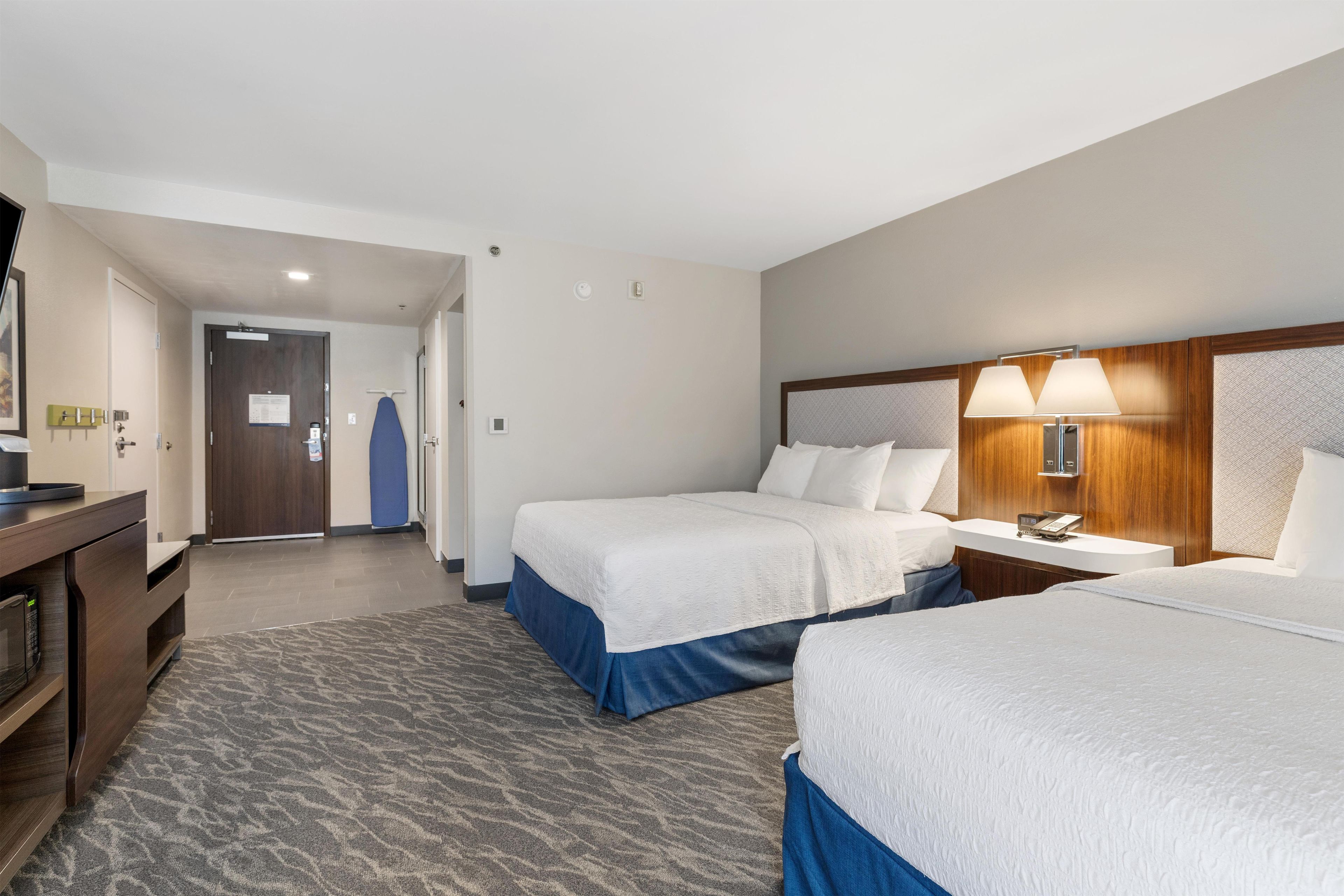 Une chambre d’hôtel avec deux lits, un bureau, une chaise, un miroir et un téléphone.