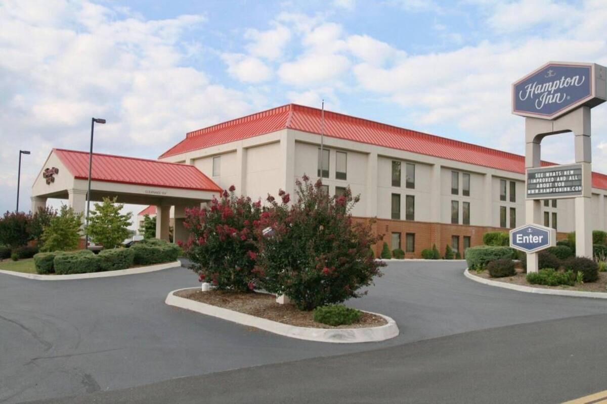 A Hampton Inn hotel with a red roof, a signboard, and a landscaped entrance area.