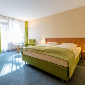 A hotel room with a bed, a chair, a table, and a lamp.