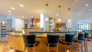 A bar area with a curved counter, black bar stools, and pendant lighting. - Schlosspark (Berlin)
