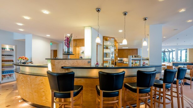 A bar area with a curved counter, black bar stools, and pendant lighting. - Schlosspark (Berlin)