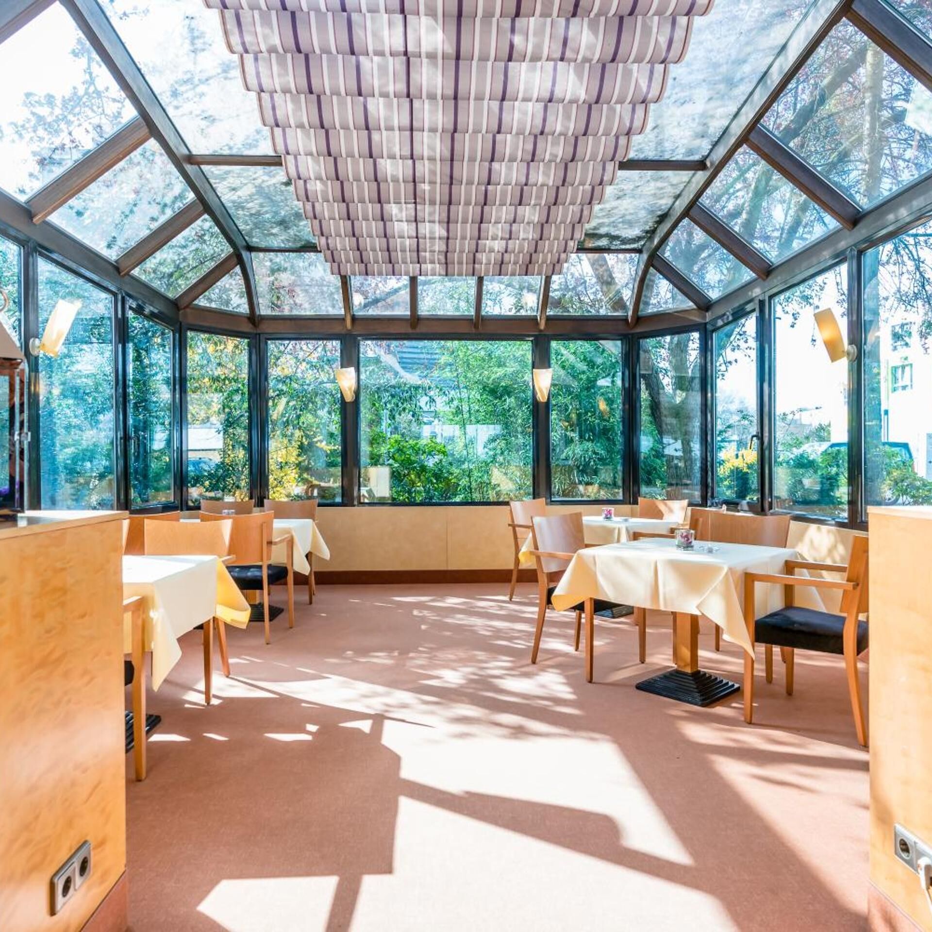 Een restaurant met een glazen plafond, tafels met witte tafellinnen en stoelen.