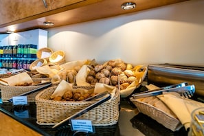 A buffet with various breads and pastries, including croissants and butter, arranged on a counter.