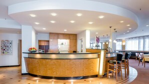 A modern hotel lobby with a curved reception desk, a kitchen area, and a seating area with chairs and tables. - Schlosspark (Berlin)