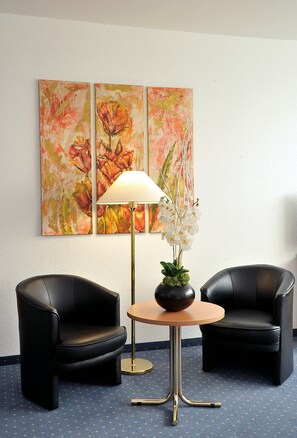 A room with two black leather chairs, a round table with a lamp, and a vase with white flowers.