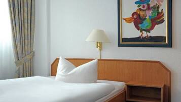 A hotel room with a bed, a nightstand, a lamp, and a colorful painting on the wall.