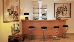 A bar area with a wooden counter, four bar stools, and two framed elephant paintings on the walls. - Hotel Ludwig van Beethoven (Berlin)