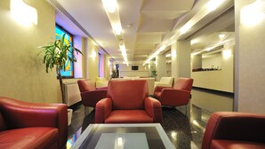 Un hall de hotel con sillones de cuero rojo, una mesa con superficie de vidrio y un ventanal con un diseño de vitral.