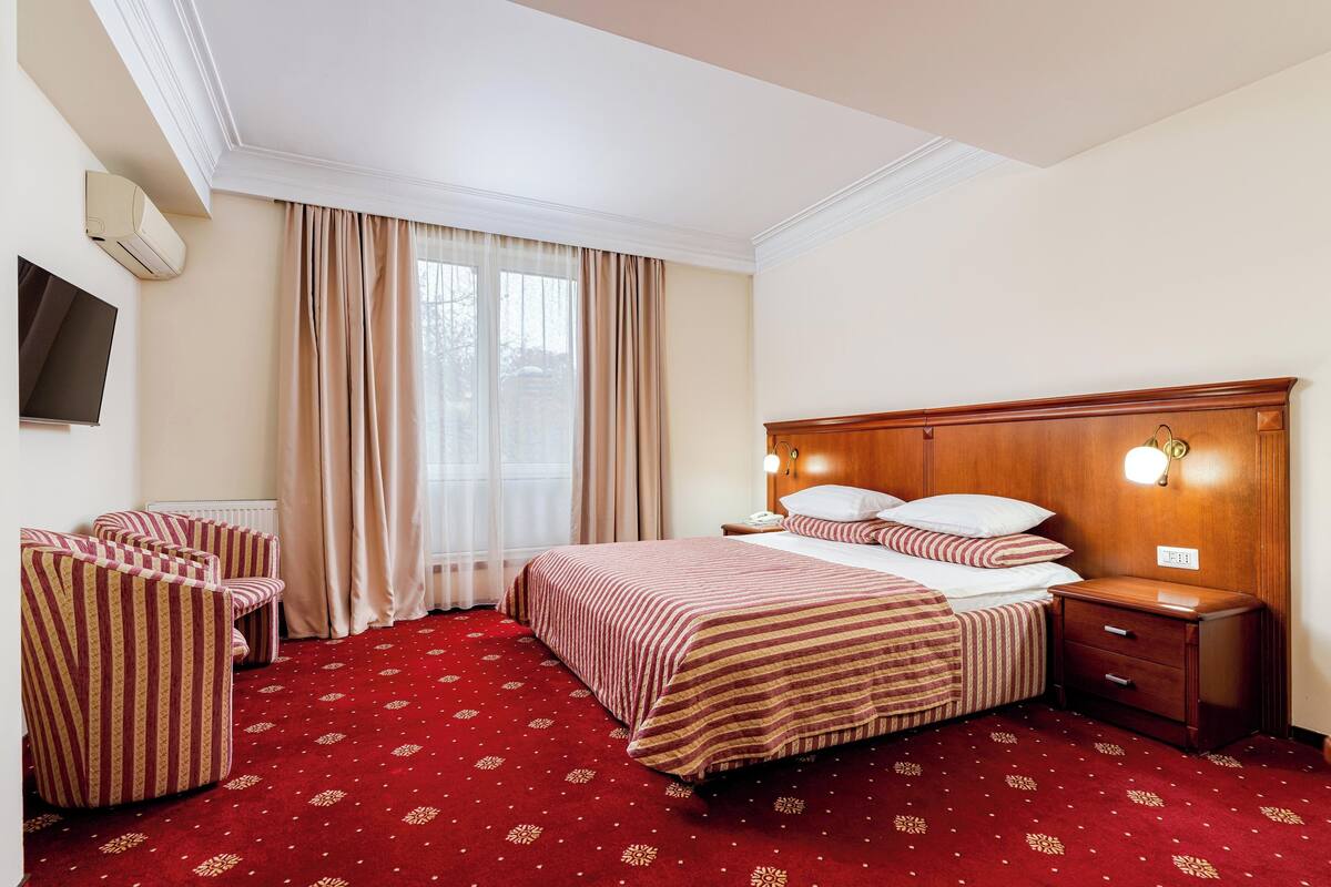 A hotel room with a bed, bedside table, lamp, and a TV on the wall.