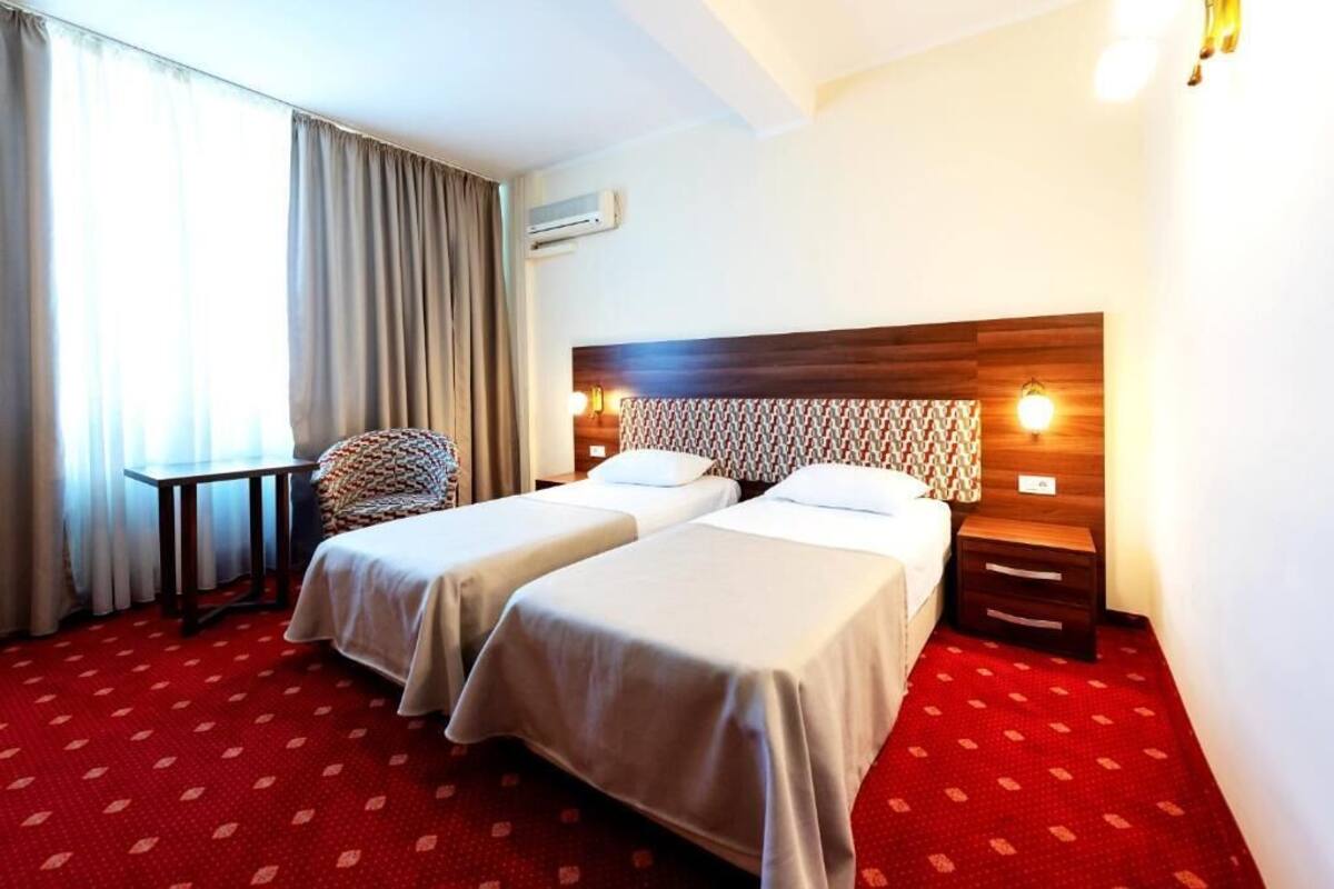 A hotel room with two beds, a small table, a chair, and a wooden headboard with a patterned design.