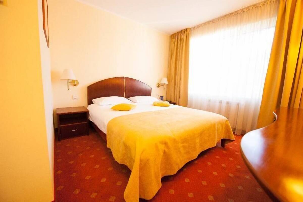 A hotel room with a bed, bedside tables, lamps, and a window with curtains.