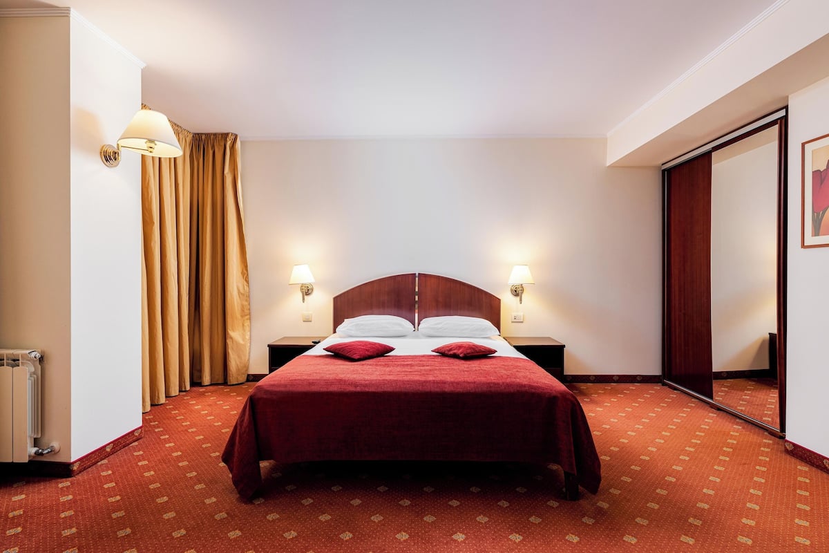 A hotel room with a large bed, two bedside lamps, a radiator, and a mirror.