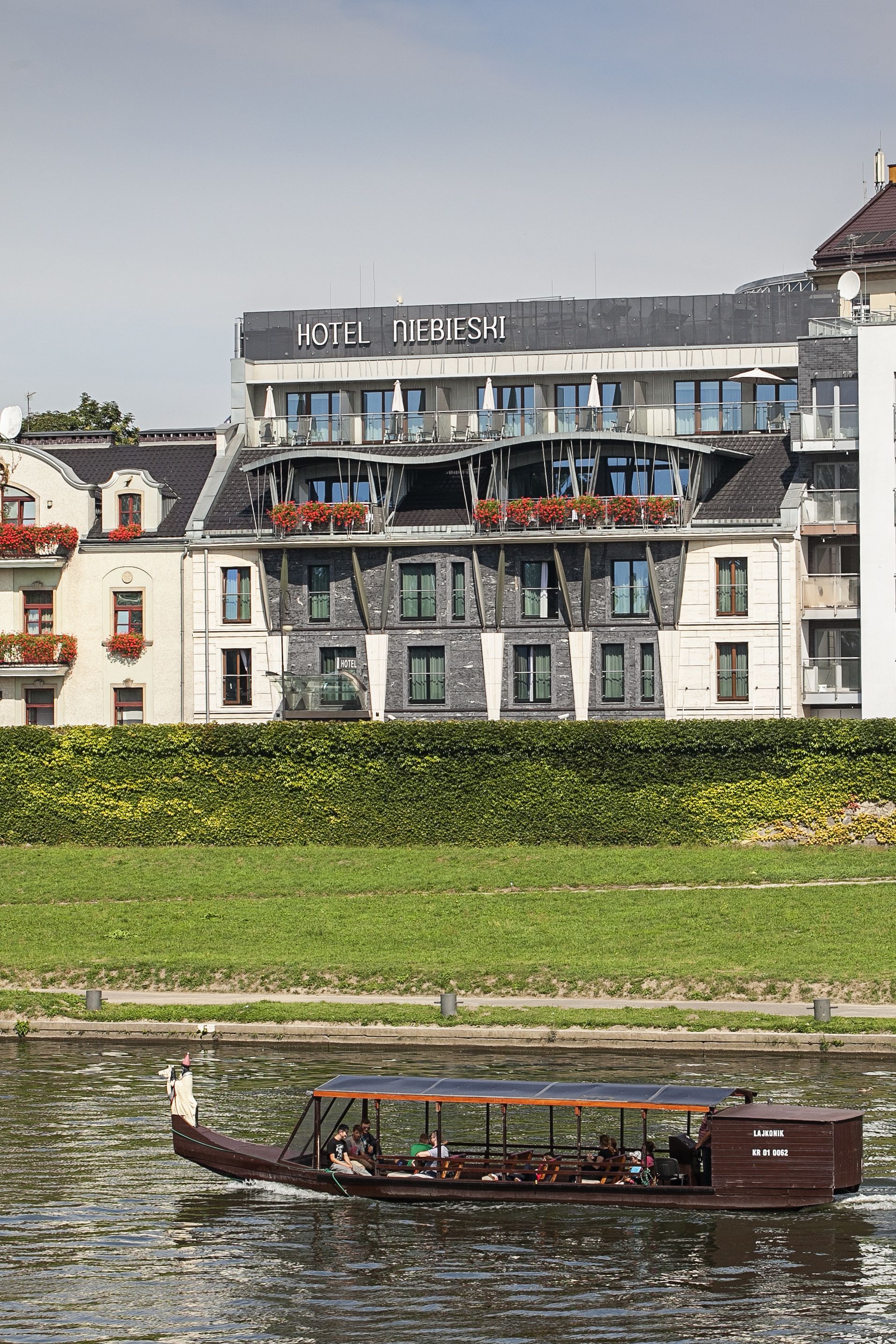 Un hotel con fachada moderna, ventanas grandes y balcones con flores rojas.