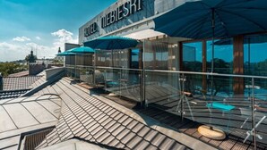 Un hotel de diseño moderno, con una terraza en la azotea que tiene barandillas de vidrio y sombrillas azules.