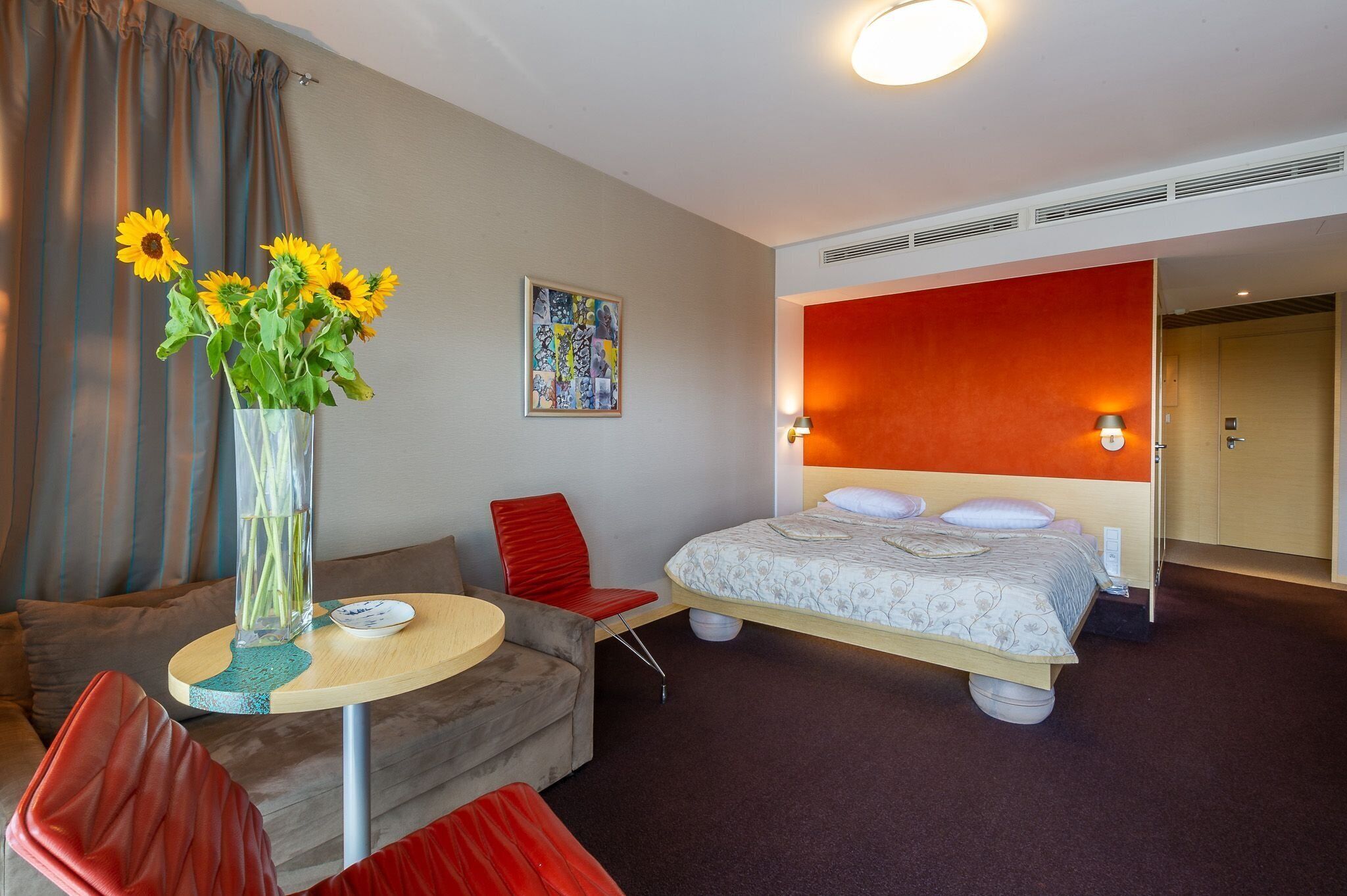 Een hotelkamer met een bed, een slaapbank, een bijzettafeltje en een vaas met zonnebloemen.