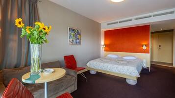 Een hotelkamer met een bed, een slaapbank, een bijzettafeltje en een vaas met zonnebloemen.
