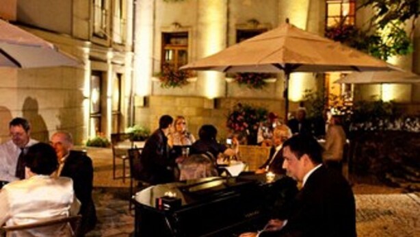 Un área de comedor al aire libre con un piano, mesas y sombrillas.