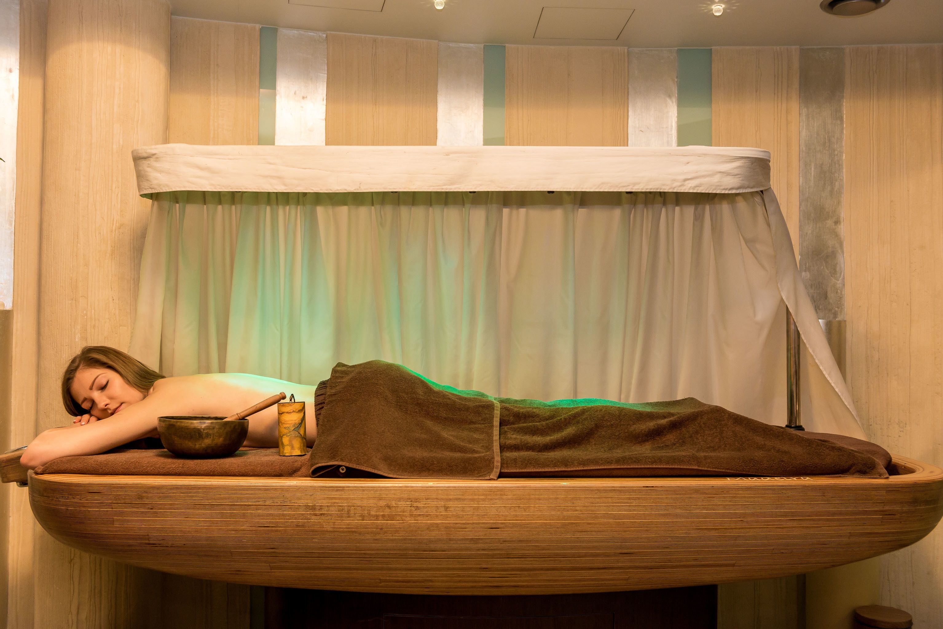 A wooden boat-shaped bed with a person lying on it, a bowl, and a cup.