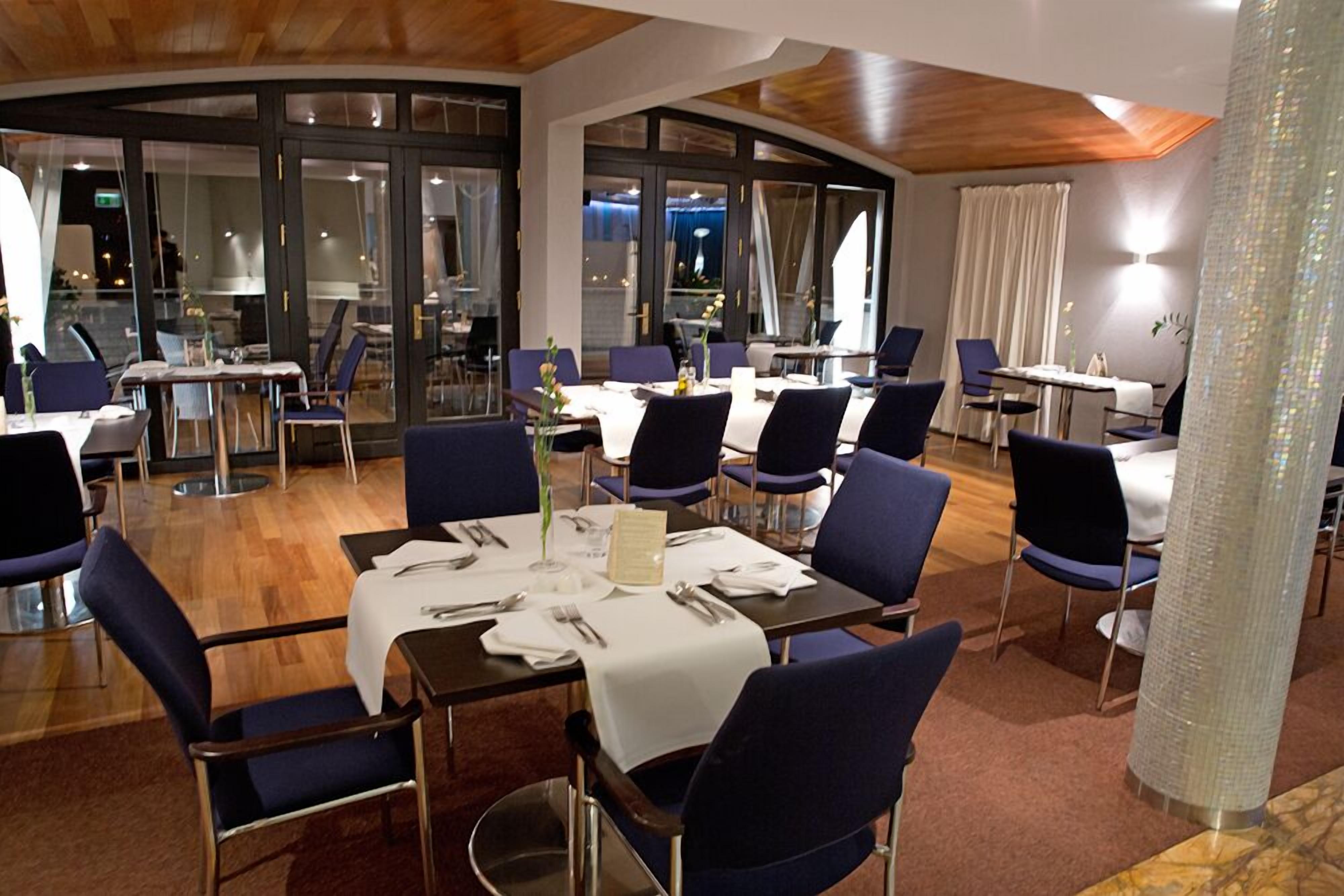 A restaurant with round tables, blue chairs, and a wooden ceiling.