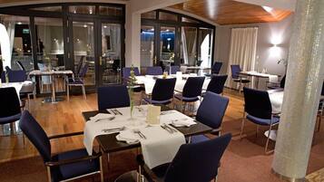 A restaurant with round tables, blue chairs, and a wooden ceiling.