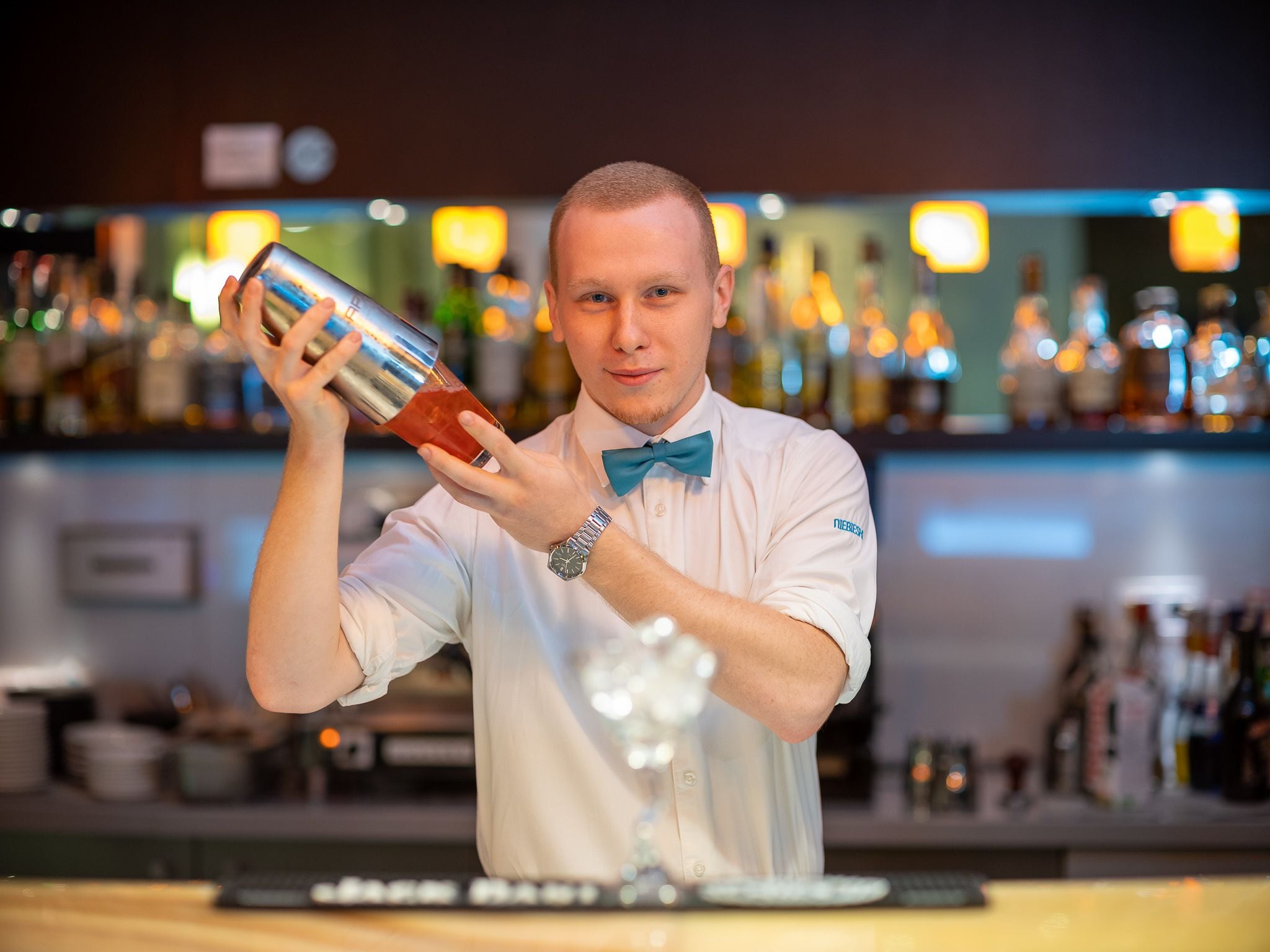 Un barman darrere de la barra, amb una varietat de garrafes al fons.