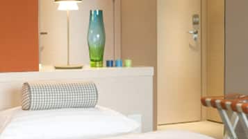 A hotel room with a bed, a bedside table with a lamp, a green vase, and a plate with croissants.