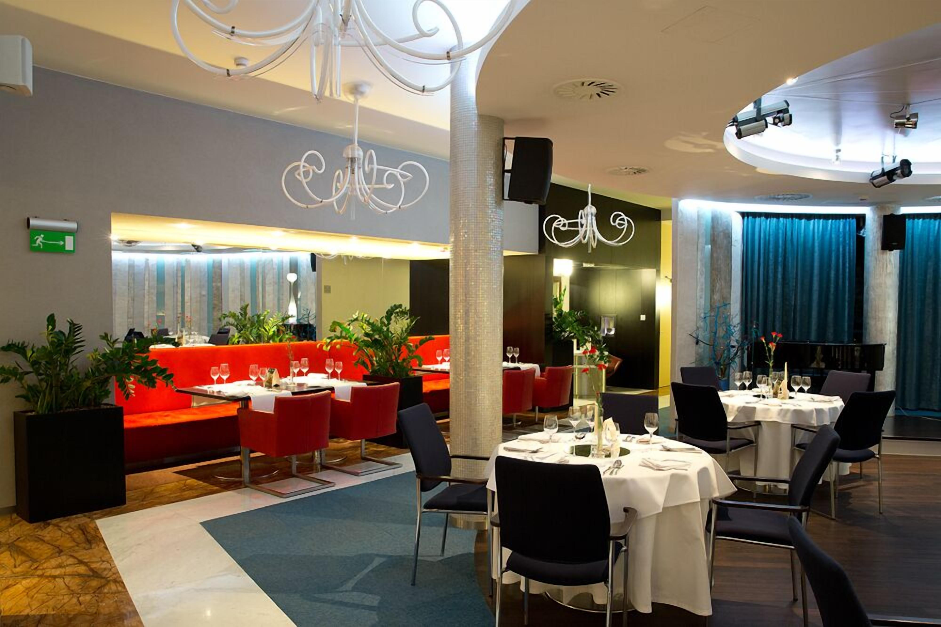 A modern restaurant with red seating, white tables, and a chandelier.