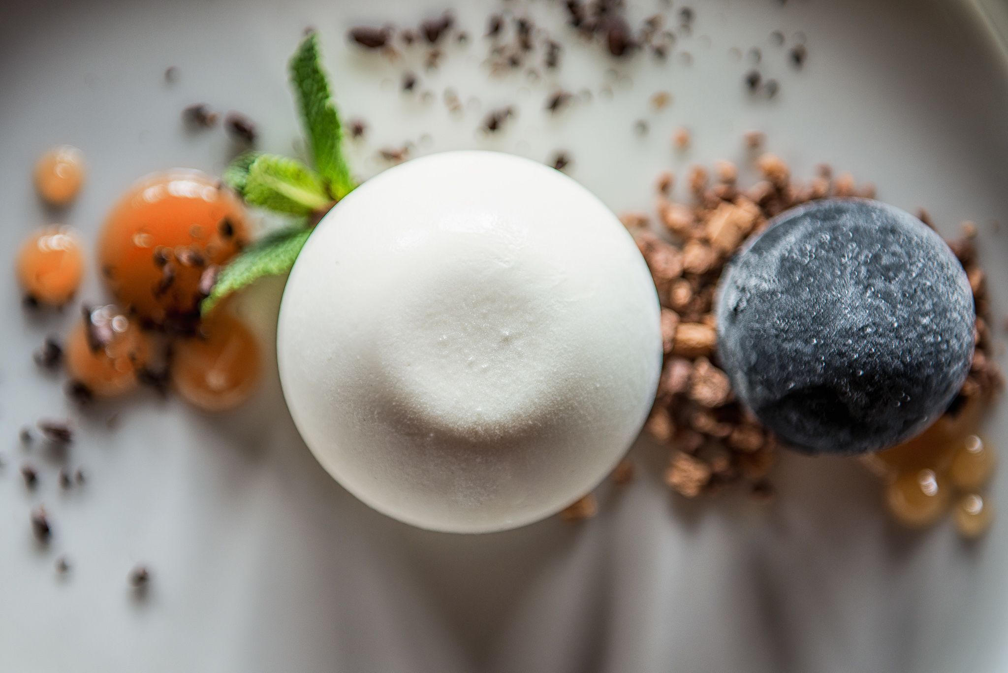 Ein Dessert mit einer weißen Kugel, Blaubeeren und orangen Kugeln auf einem Teller.