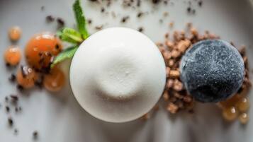 Ein Dessert mit einer weißen Kugel, Blaubeeren und orangen Kugeln auf einem Teller.